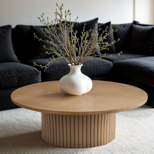 The round Grove Coffee Table with a ribbed pedestal base in a dark living room, styled with a vase against a black sectional sofa.