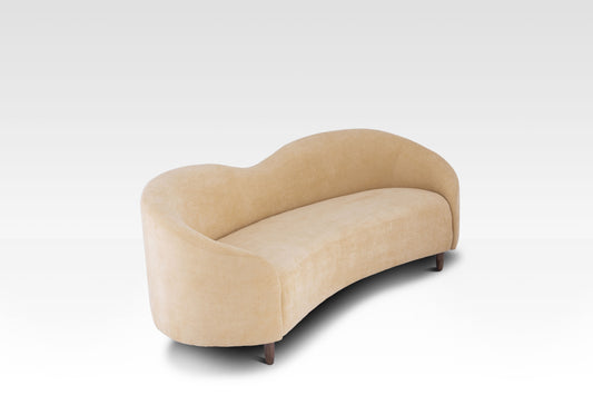 A high-angle view of the Aaria sofa showing its unique curved kidney-bean shape and soft cream fabric.