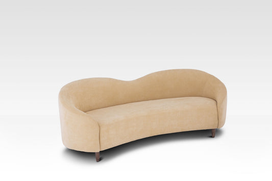 An angled view of the Aaria curved sofa in cream velvet, showing its rounded shape and soft fabric.