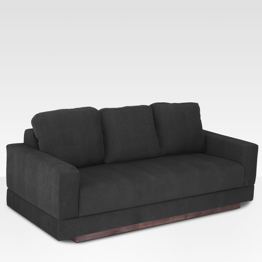 An angled view of the Kyra sofa highlighting the seamless bench seat, wide track arms, and the architectural wood base.