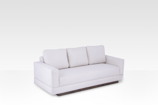 An angled perspective of the Kyra sofa highlighting its low profile, soft cream fabric, and rich walnut-toned wood plinth base.