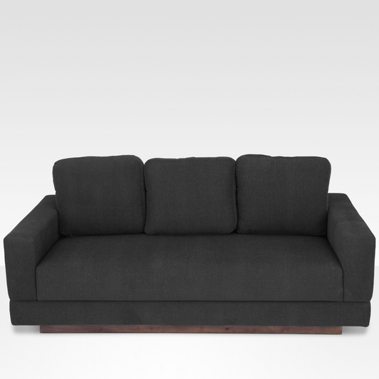 A front view of the Kyra sofa in Pewter gray fabric, showing the three back cushions, seamless bench seat, and solid wood plinth base.