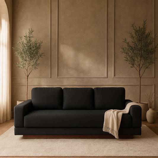 A centered view of the Kyra sofa in Pewter gray against a textured taupe wall, styled with twin olive trees and a cream throw blanket.