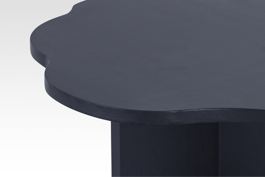 Macro close-up of the Nook Nestled Coffee Table in matte black, showing the natural wood grain texture and the smooth, rounded wavy edge.
