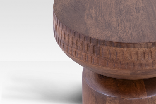 A macro detail of the Orbit End Table’s center, highlighting the intricate, rhythmic hand-carved ridges and the natural warmth of the mango wood.